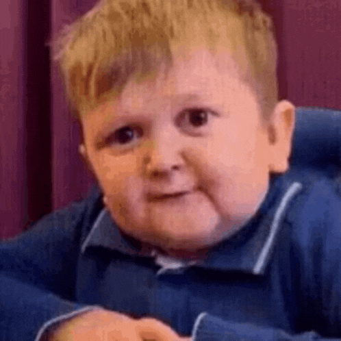 a little boy in a blue shirt is sitting in a high chair making a funny face .