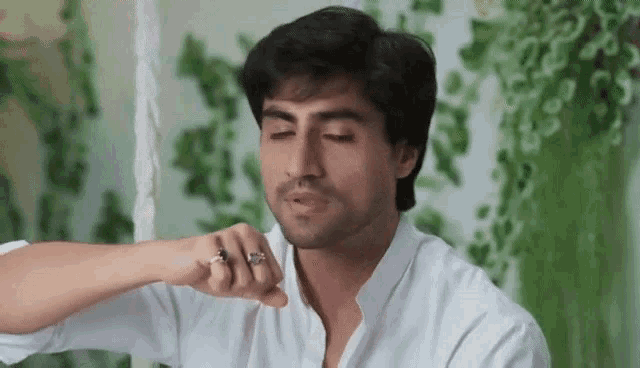 a man wearing a white shirt and a ring is smoking a cigarette .