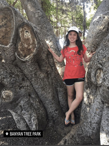 a girl in a red shirt is standing next to a tree with banyan tree park written on the bottom