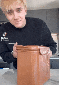 a man wearing a black shirt that says tiktok is holding a brown container