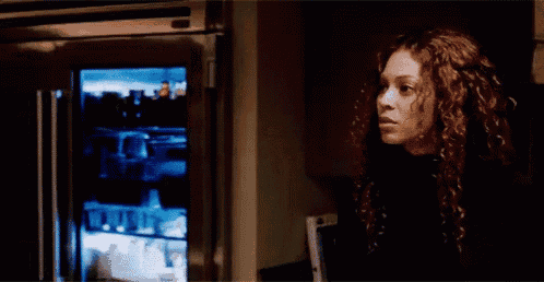 a woman with curly hair is standing in front of a refrigerator with a glass door .