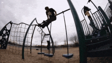 a man in a black shirt is sitting on a swing set in a playground