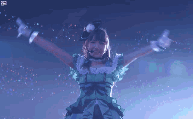 a girl in a green dress is dancing with her arms outstretched on a stage