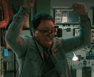 a man wearing glasses is raising his arms in the air in front of a computer monitor