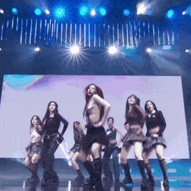a group of women are dancing on a stage with a large screen in the background