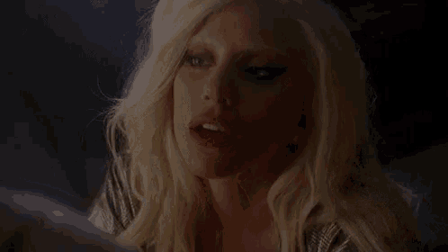 a close up of a woman with blonde hair and red lips looking at a mirror .