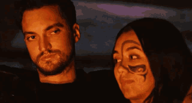 a man and a woman are posing for a picture with the woman having a tattoo on her face