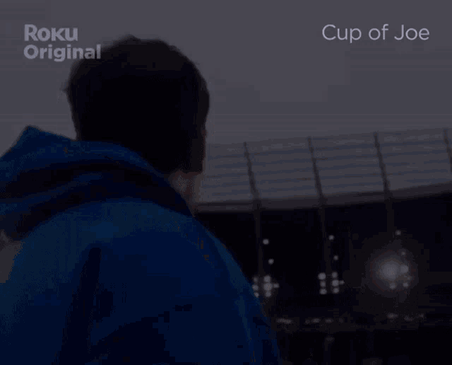 a man in a blue hoodie is standing in front of a stadium with the words cup of joe on the screen