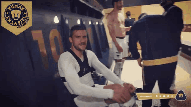 a man sitting in a locker room with the pumas logo on the wall
