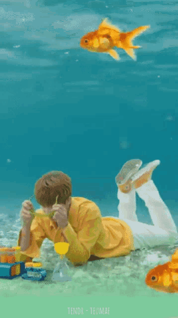 a boy in a yellow shirt is laying on the ground in the water