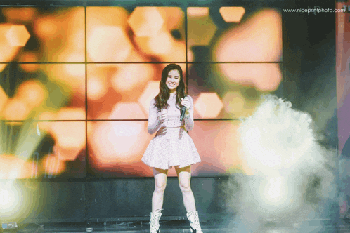 a girl in a pink dress is holding a microphone in front of a wall that says www.niceprintphoto.com on it