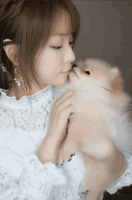 a woman in a white dress is kissing a small brown dog