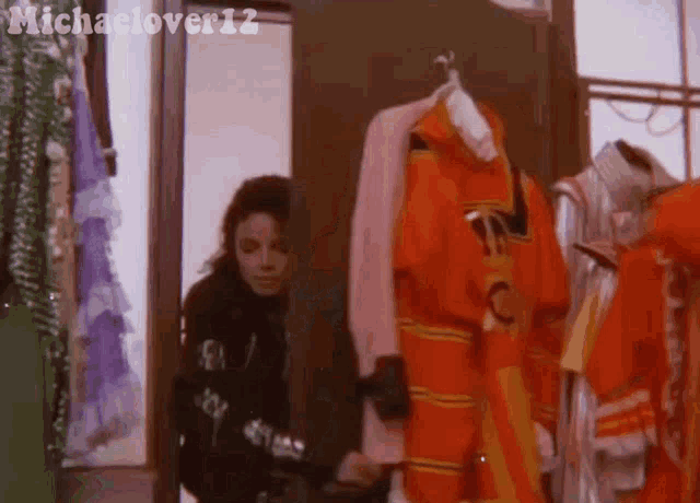 a woman in a black jacket is standing in a room with clothes hanging on racks .