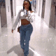 a woman is walking down a hallway wearing a white crop top and blue jeans .