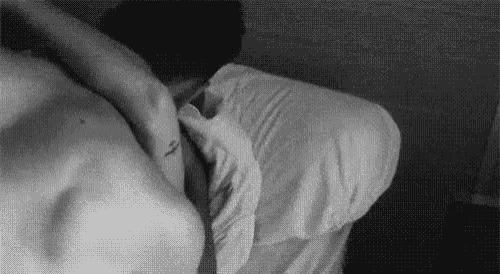 a black and white photo of a man laying on a bed with his arm around another man 's shoulder .