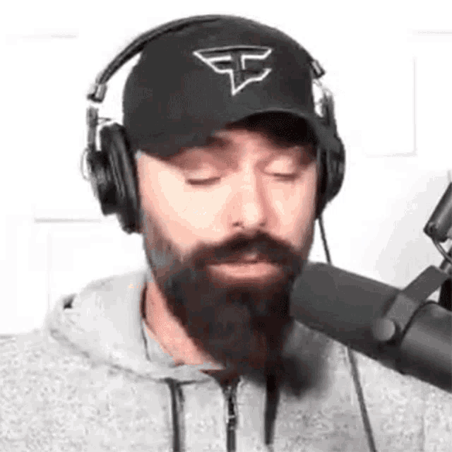 a man with a beard is wearing headphones and a hat while speaking into a microphone .