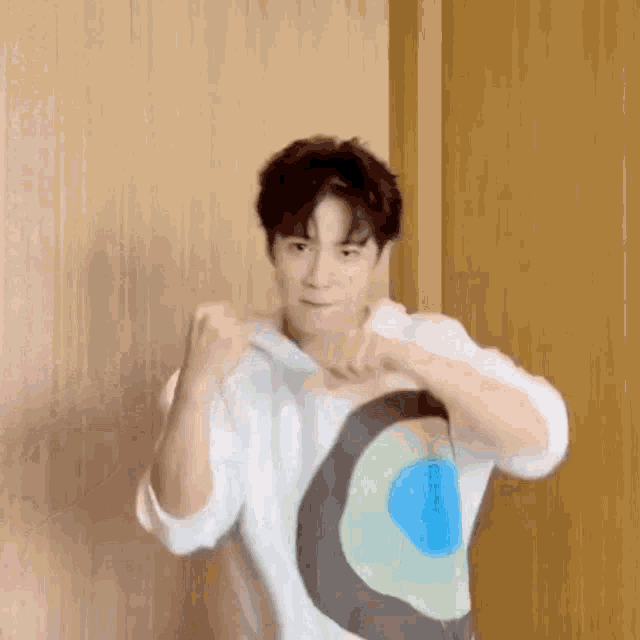 a young man is standing in front of a wooden wall wearing a white shirt with a circle on it .
