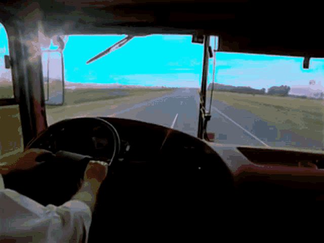 a man is driving a bus down a highway with a field in the background