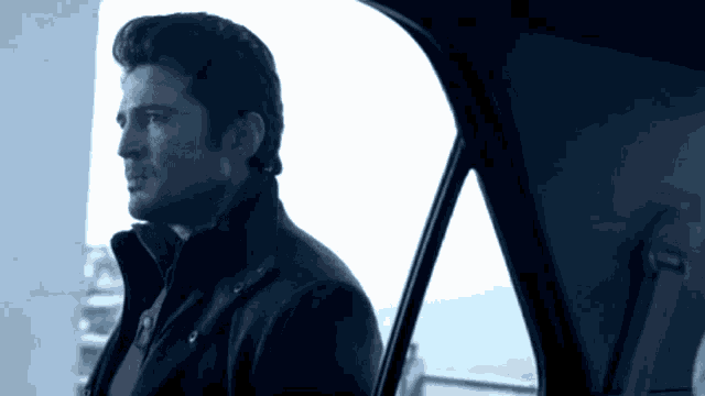 a man in a black jacket is looking out the window of a car