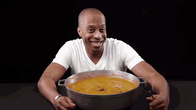 a man is holding a pot of soup and smiling