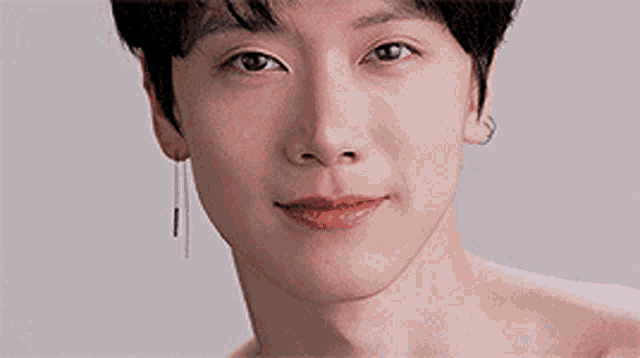 a close up of a young man 's face wearing earrings and smiling .