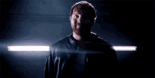 a man in a leather jacket is standing in a dark room with a light shining on him .