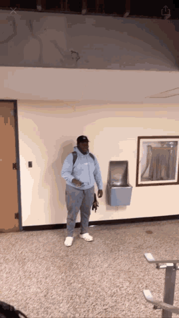 a man in a blue hoodie stands in a hallway