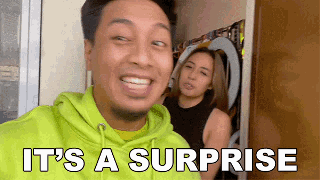 a man in a green hoodie says it 's a surprise in front of a woman