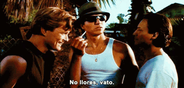 a man in a white tank top says no llores vato while smoking a cigarette