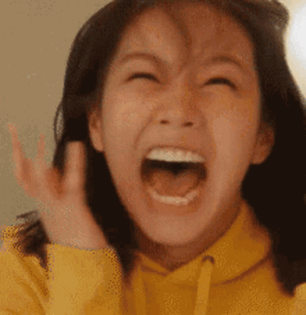 a woman in a yellow hoodie is making a funny face with her mouth open