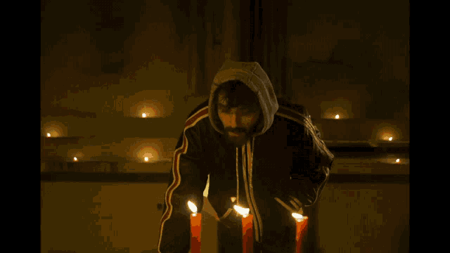 a man in a hooded jacket is lighting candles in the dark