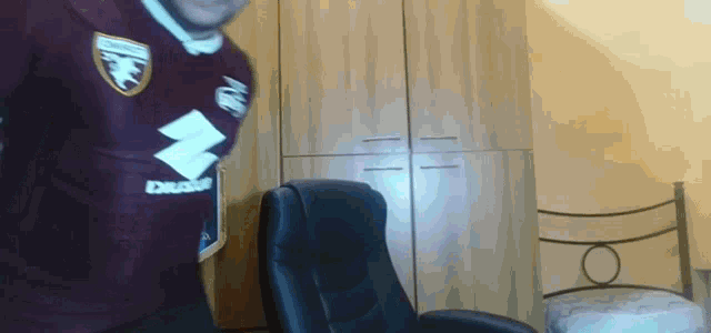 a man in a maroon shirt with a suzuki logo is standing in front of a chair