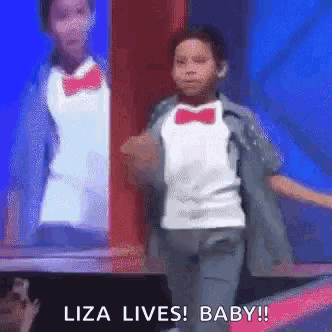 a young boy in a tuxedo and bow tie is dancing on a stage and says `` liza lives ! baby ! ''
