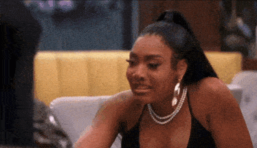a woman in a black top and pearl necklace is crying while sitting on a couch .