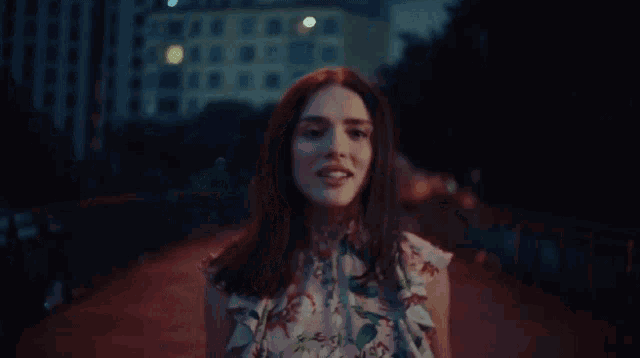 a woman in a floral top smiles while walking on a bridge