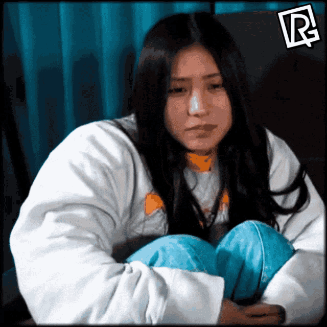 a woman in a white jacket sits with her knees crossed and a r on the bottom right