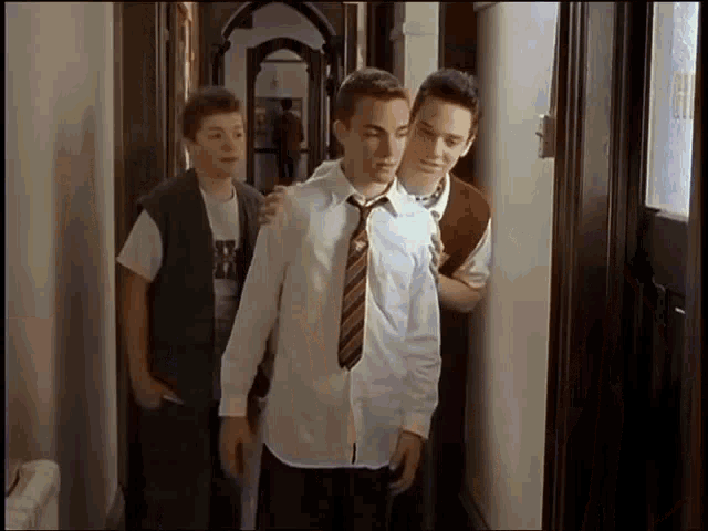 three young men are standing in a hallway and one of them is wearing a tie