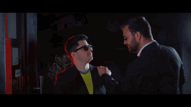 a man wearing sunglasses and a suit has the name alex on the bottom