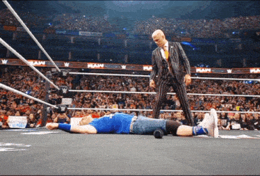 a man in a suit is standing next to a wrestler laying on the ground