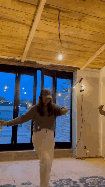 a woman is dancing in a room with a wooden ceiling and a large window