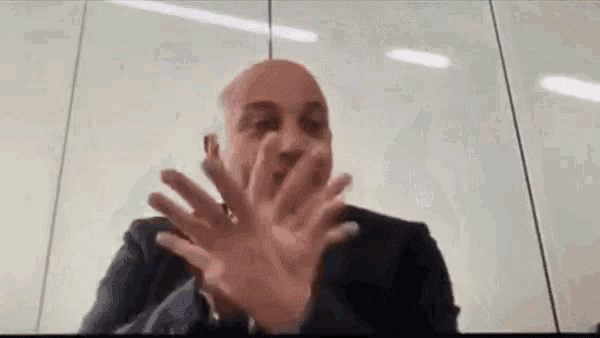 a bald man in a suit is making a funny face while sitting in front of a computer screen .