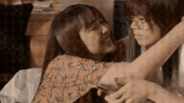 two women are hugging each other and one is holding a cell phone in her hand .
