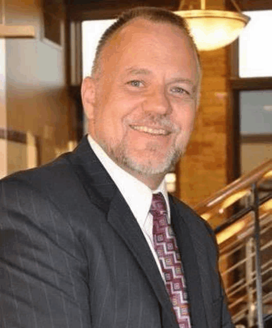 a man in a suit and tie is smiling for the camera while standing in front of a staircase .