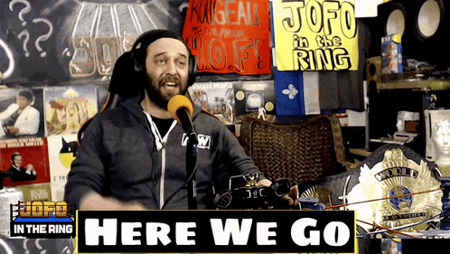 a man speaking into a microphone with a sign that says here we go