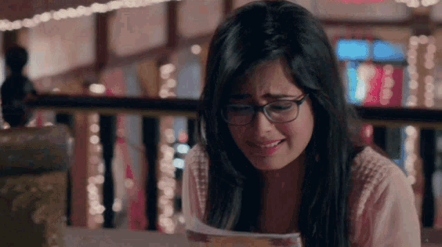 a woman wearing glasses is crying while reading a magazine