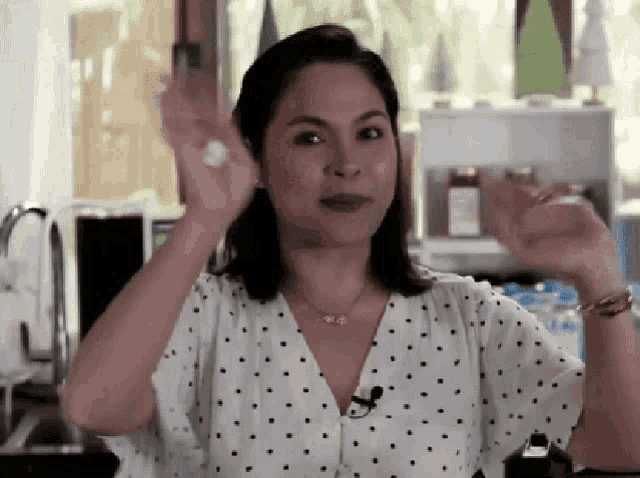 a woman wearing a white polka dot shirt is making a funny face