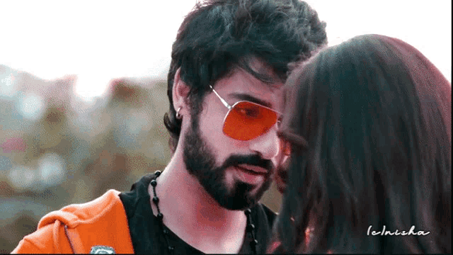 a man with a beard wearing red sunglasses looks at a woman 's face