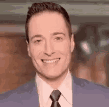a man in a suit and tie is smiling while standing in front of a camera .