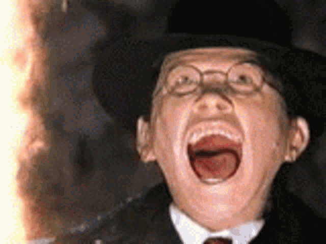 a man wearing a top hat and glasses is screaming in front of a fire .