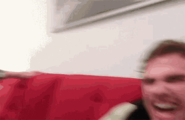 a blurry picture of a man sitting on a red couch with a remote control in his hand .
